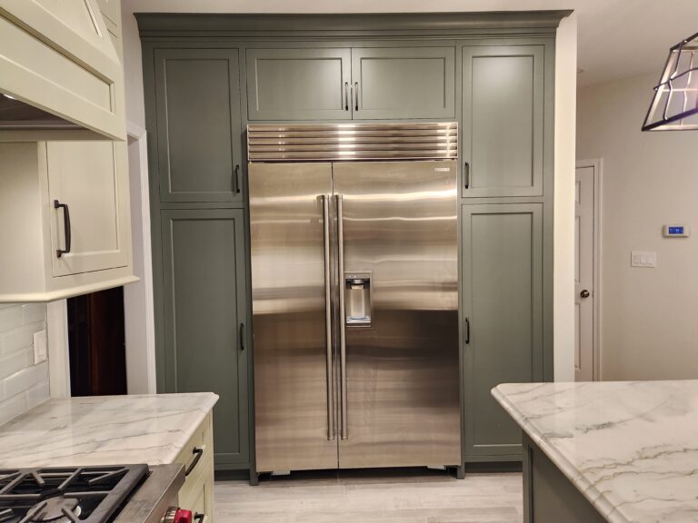 A Kitchen With Large Island And Sink That Has A Granite Countertop, And White And Gray Cabinets With Custom Trim