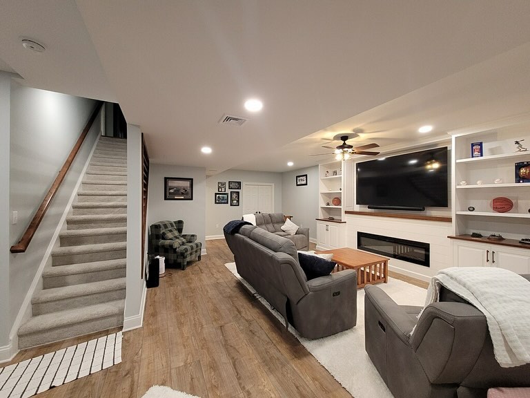 A Newly Finished Basement With Comfy Couches, Brand New Lighting, Walls, And A Stripe Design On The Staircase Wall, With An Area For Games In The Back, Such As Table Tennis And Foosball, In Chester County Pa