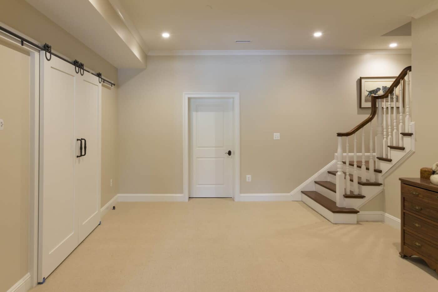 A Clean, Newly Finished Basement Area With Tan Walls And A Tan Floor, A Staircase Leading In From Upstairs, A Regular Door, And A Sliding Closet Door In Gladwyne, Pa