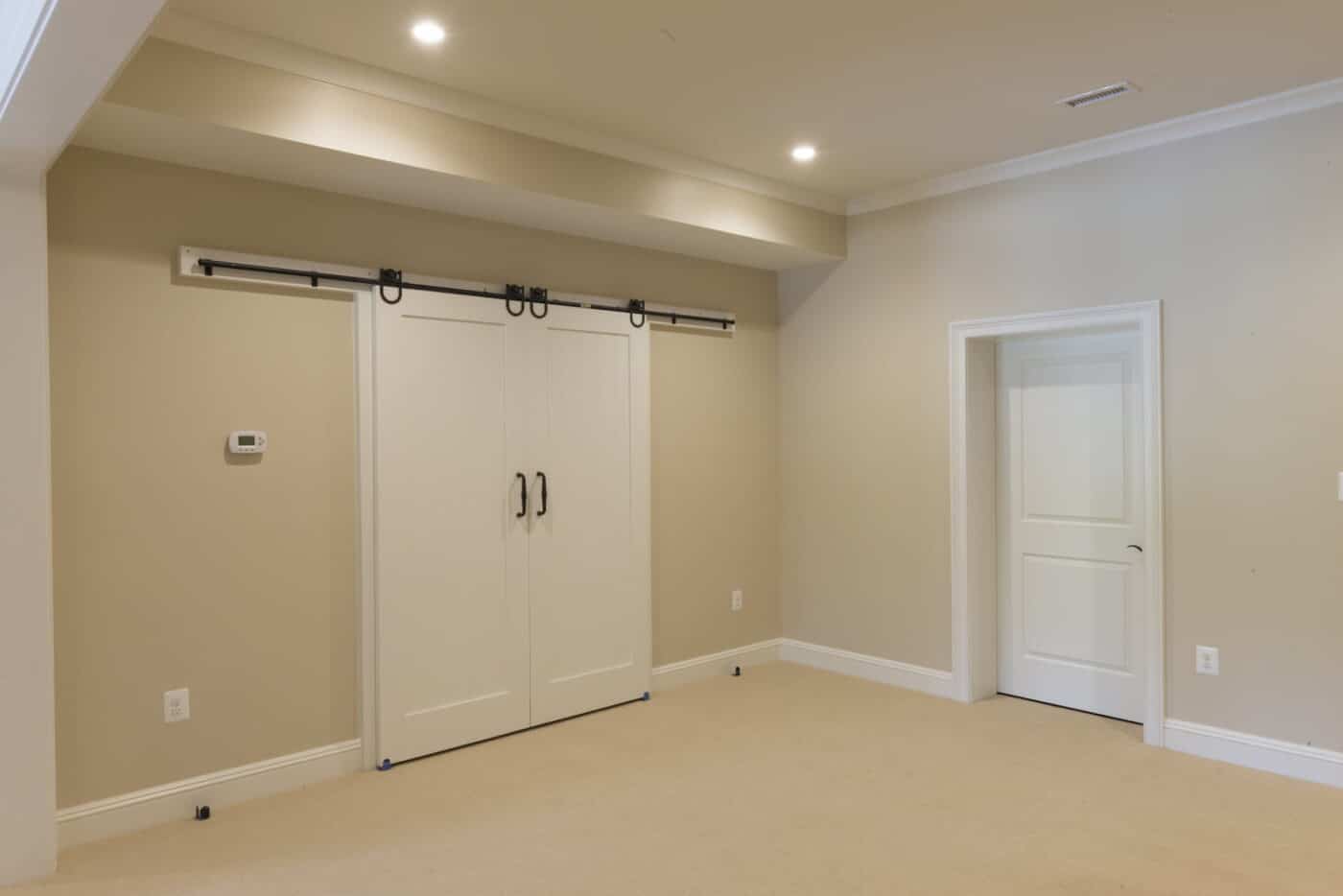 A Clean, Newly Finished Basement Area With Tan Walls And A Tan Floor, A Regular Door, And A Sliding Closet Door In Glen Mills, Pa