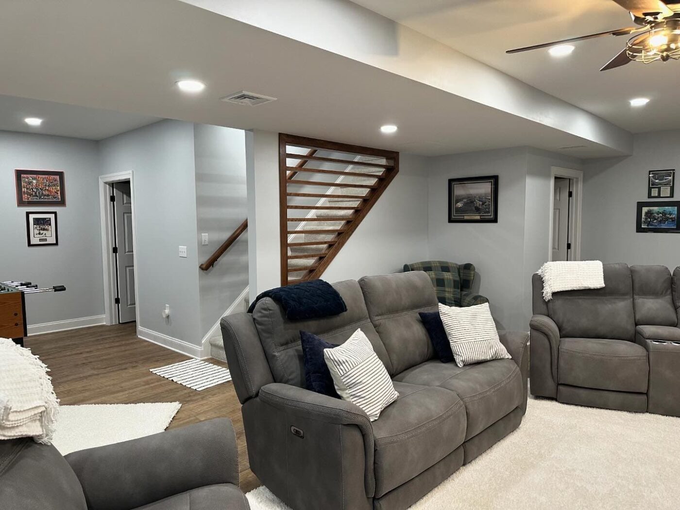 A Newly Finished Basement With Comfy Couches, Brand New Lighting, Walls, And A Stripe Design On The Staircase Wall, With An Area For Games In The Back, Such As Table Tennis And Foosball, In Merion Station Pa