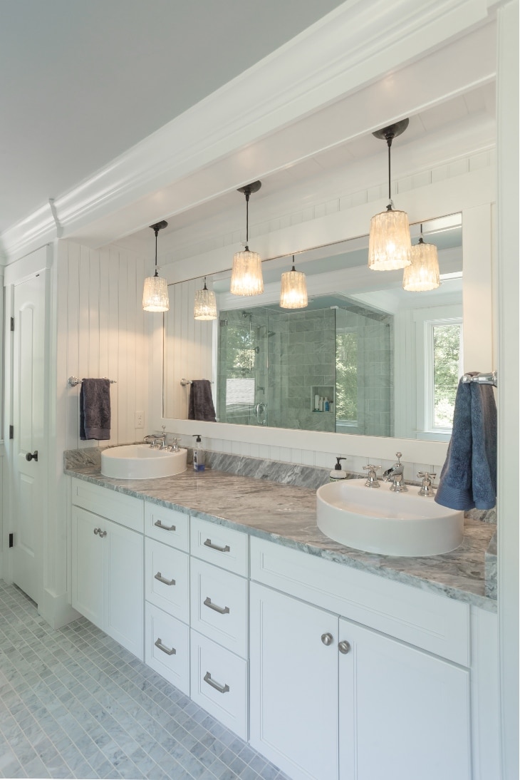 A Bathroom With A Wide Mirror, Overhead Lights And Two Sinks