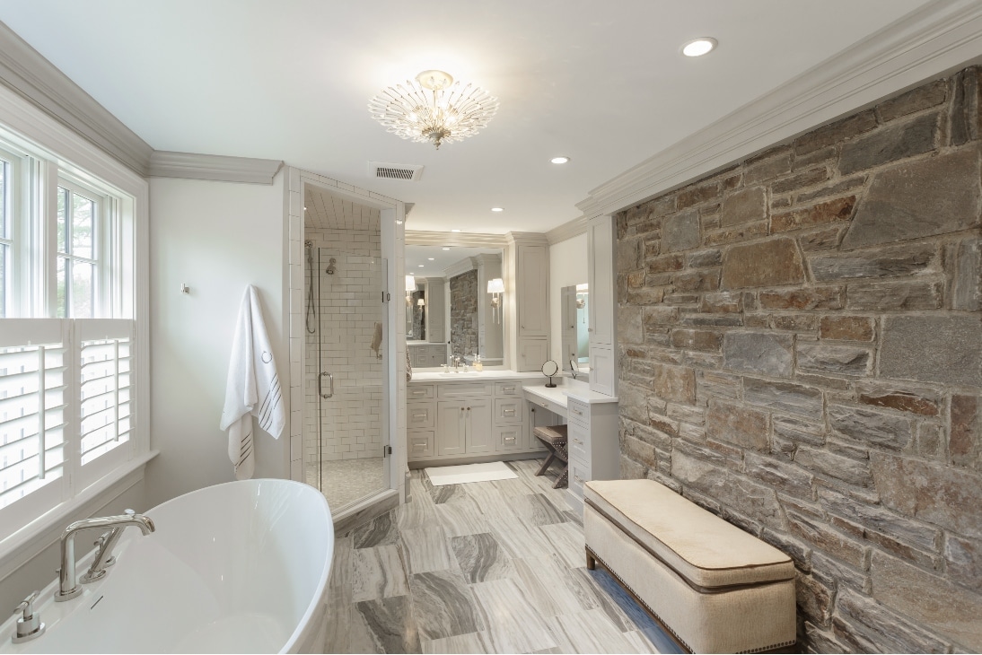 A Newly Remodeled Bathroom With A Stone Brick Wall, A Classic Looking Bath Tub, And A Seat In Radnor Pa