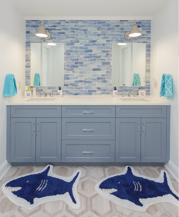 A Remodeled Bathroom With A Pretty Blue And White Backsplash, Two Sinks And Mirrors, And Two Blue/White Rugs Shaped Like Sharks In Ardmore Pa