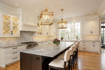 A Kitchen With White Cabinets, A White Backsplash With Gold Geometric Patterns, A Large Island With A Gray Countertop, Wood Sides, And Four White Chairs, Remodeled By Foggy Ridge, Custom Kitchen Remodelers In Lancaster, Pennsylvania.